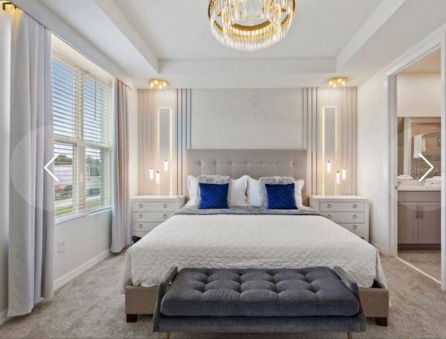 carpeted bedroom with a tray ceiling, multiple windows, ensuite bath, and a chandelier