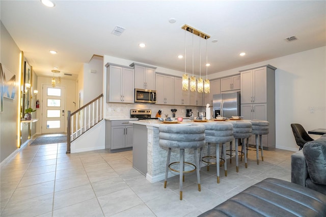 kitchen with gray cabinets, stainless steel appliances, decorative backsplash, a center island with sink, and a kitchen breakfast bar