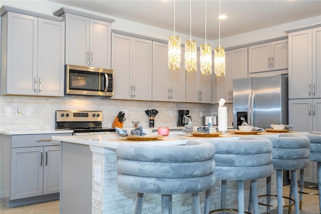 kitchen featuring appliances with stainless steel finishes, a breakfast bar area, an island with sink, and gray cabinetry