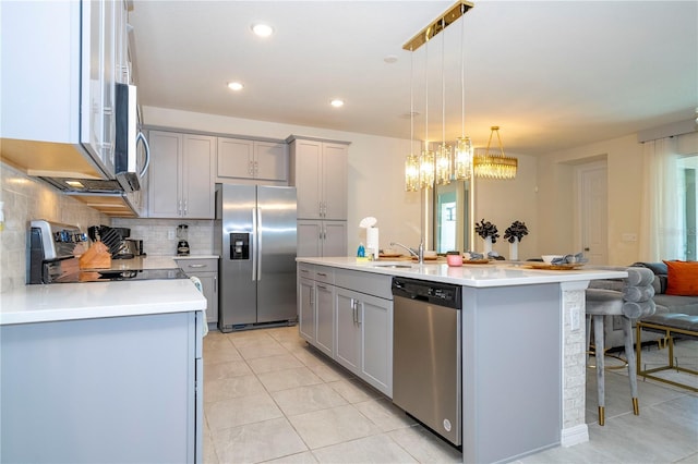 kitchen featuring gray cabinets, appliances with stainless steel finishes, backsplash, and a kitchen island with sink