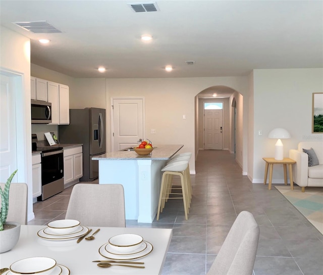 kitchen featuring white cabinets, light stone counters, a kitchen bar, a center island, and stainless steel appliances