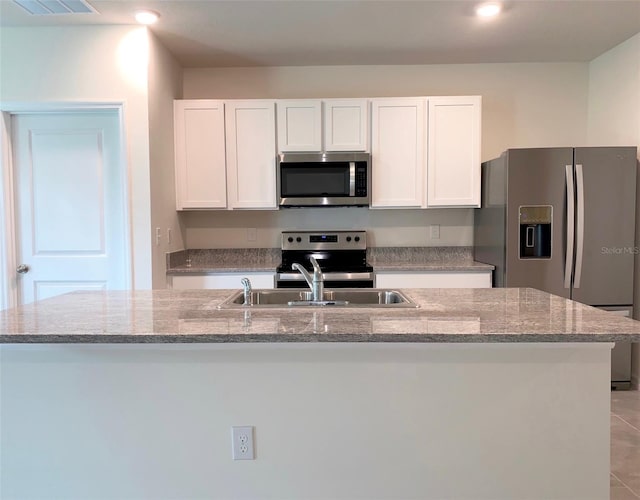 kitchen with light stone countertops, white cabinets, stainless steel appliances, and a kitchen island with sink