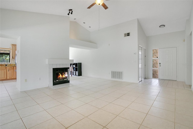 unfurnished living room with ceiling fan, high vaulted ceiling, a tile fireplace, and light tile patterned floors