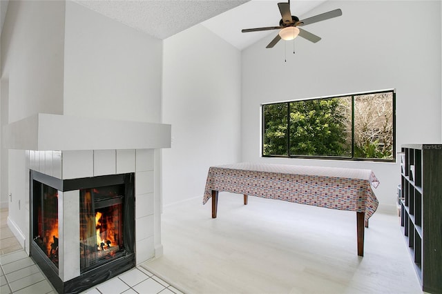 living room featuring lofted ceiling, light tile patterned floors, a tile fireplace, ceiling fan, and a textured ceiling