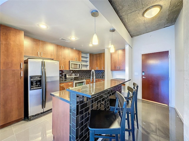 155 S Court Ave Unit 1610, Orlando, FL 32801 - kitchen featuring stainless steel appliances, brown cabinets, decorative backsplash, a kitchen bar, and hanging light fixtures