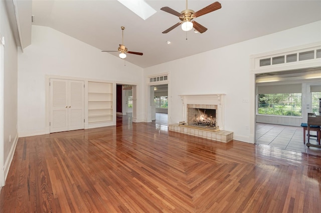 unfurnished living room featuring tile patterned flooring, a tiled fireplace, a skylight, high vaulted ceiling, and ceiling fan