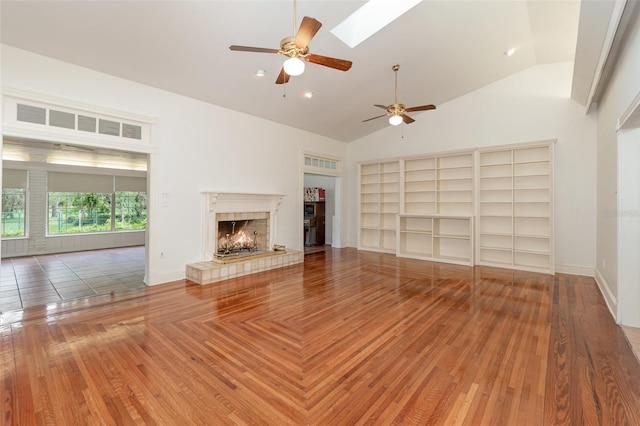 unfurnished living room with built in shelves, vaulted ceiling with skylight, a tiled fireplace, and hardwood / wood-style flooring