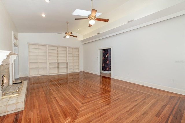 unfurnished living room featuring a brick fireplace, vaulted ceiling with skylight, ceiling fan, and built in shelves