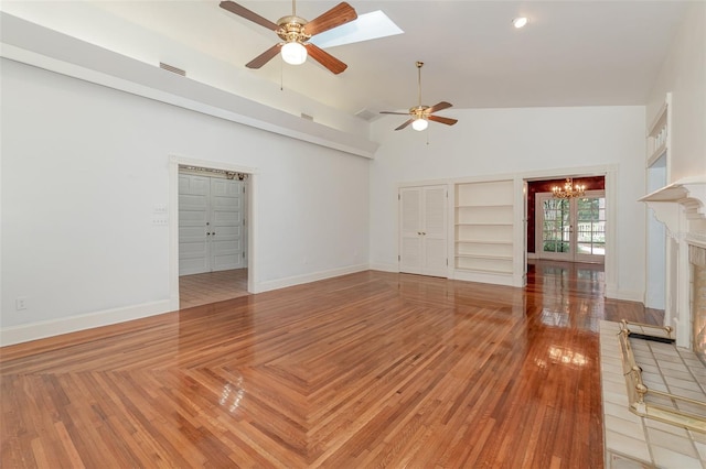 unfurnished living room featuring built in shelves, high vaulted ceiling, ceiling fan with notable chandelier, and a brick fireplace