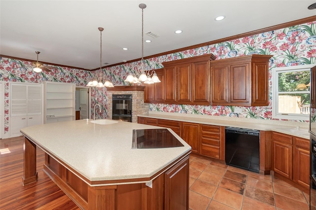 kitchen featuring sink, crown molding, a fireplace, black appliances, and a center island with sink