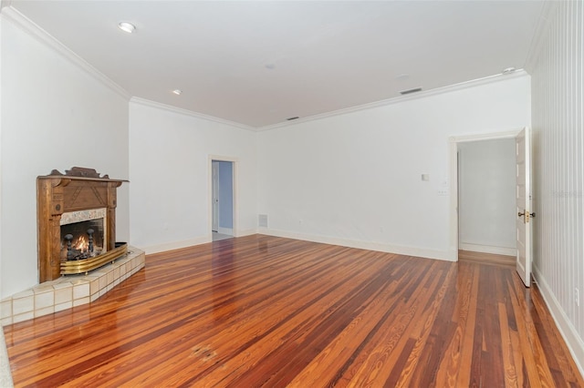 unfurnished living room featuring a tiled fireplace, ornamental molding, and hardwood / wood-style floors