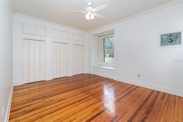 unfurnished bedroom featuring crown molding, ceiling fan, wood-type flooring, and multiple closets