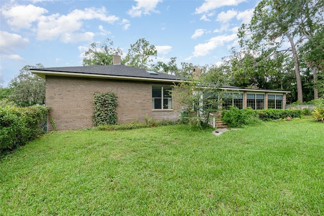 rear view of house featuring a yard and a sunroom