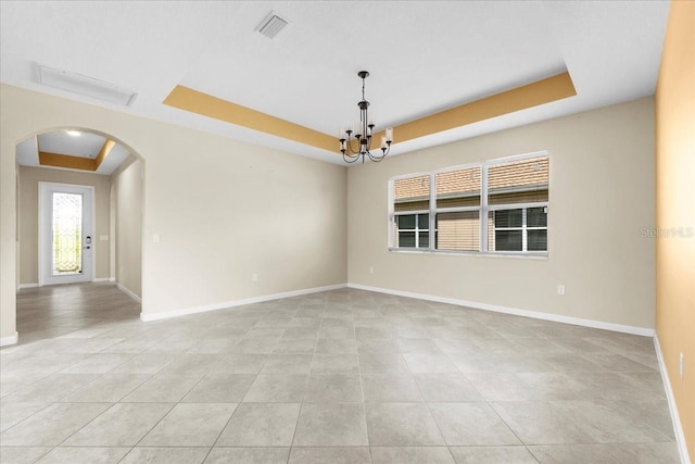 empty room with light tile patterned floors, a tray ceiling, and a chandelier