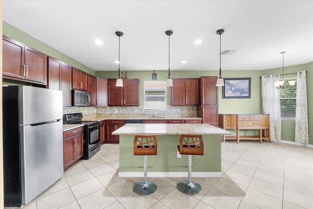 kitchen with hanging light fixtures, a kitchen breakfast bar, a center island, black appliances, and decorative backsplash