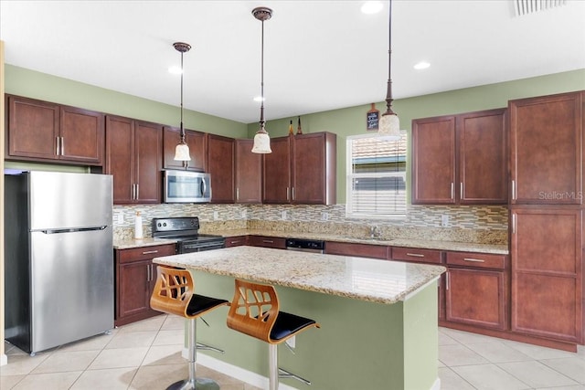 kitchen with light tile patterned floors, hanging light fixtures, stainless steel appliances, a center island, and light stone counters