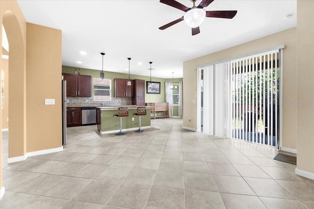 kitchen with light tile patterned flooring, a kitchen island, decorative light fixtures, dark brown cabinetry, and stainless steel appliances