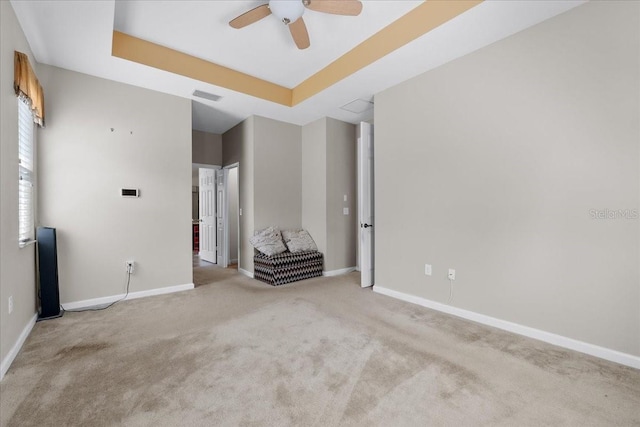 carpeted empty room with a raised ceiling and ceiling fan