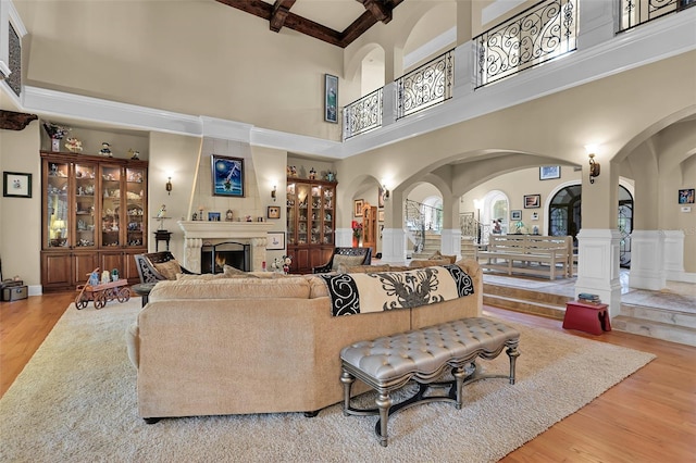 living room featuring light hardwood / wood-style flooring, beam ceiling, a towering ceiling, and a fireplace