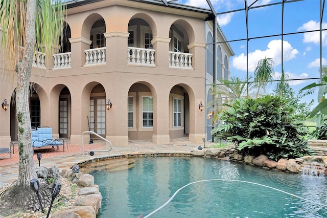 back of house with glass enclosure, a patio, and stucco siding