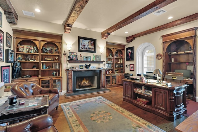 office area featuring visible vents, beamed ceiling, a warm lit fireplace, and dark wood-style floors