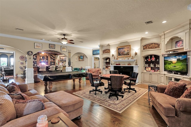 living room with wood-type flooring, built in shelves, ornamental molding, and a textured ceiling