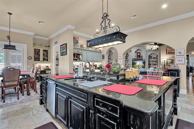 kitchen featuring hanging light fixtures, dark stone countertops, crown molding, and an island with sink