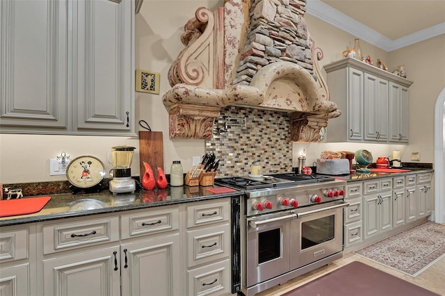 kitchen featuring dark stone counters, range with two ovens, arched walkways, crown molding, and backsplash