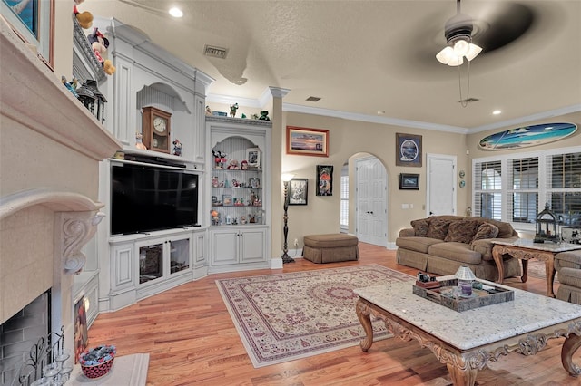 living area featuring arched walkways, a textured ceiling, light wood-style floors, and ornamental molding