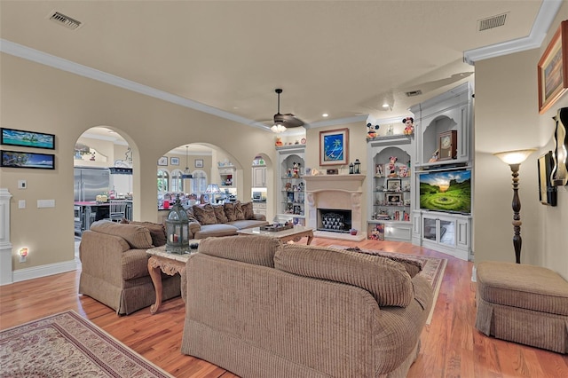 living room with ceiling fan, built in shelves, ornamental molding, and light hardwood / wood-style flooring