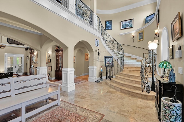 entrance foyer with stairway, arched walkways, french doors, a towering ceiling, and crown molding