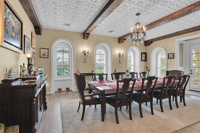 dining space with an inviting chandelier, light wood-style floors, visible vents, and beam ceiling