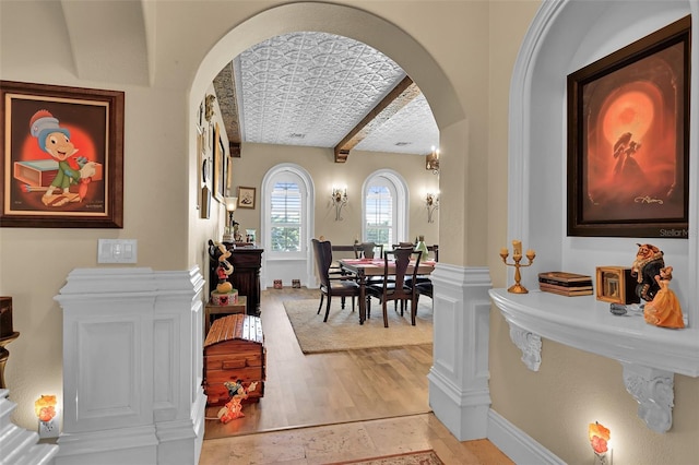 interior space with beamed ceiling, wainscoting, arched walkways, and light wood-type flooring