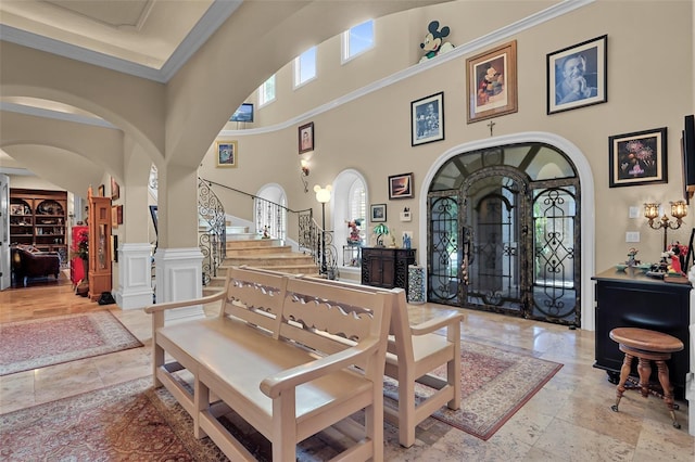 entryway with a wainscoted wall, ornamental molding, stairway, arched walkways, and a high ceiling