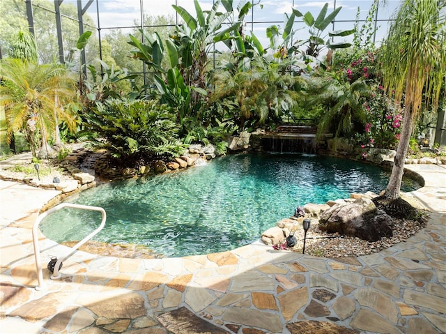 view of pool featuring pool water feature, a patio, glass enclosure, and a small pond