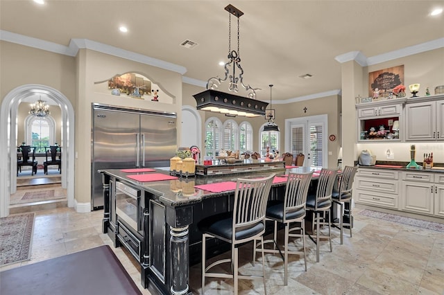 kitchen featuring visible vents, a kitchen bar, arched walkways, crown molding, and a large island with sink