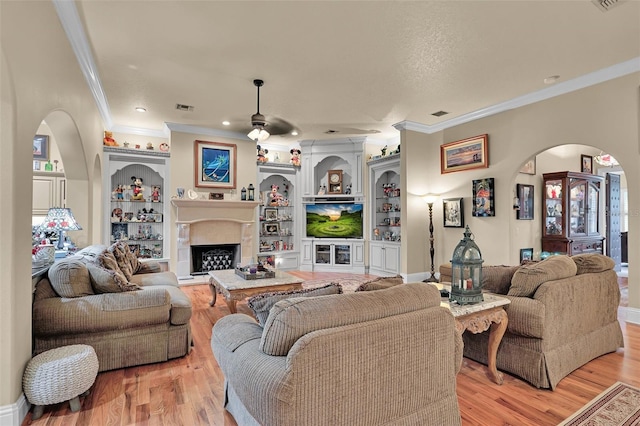 living room featuring ceiling fan, built in features, crown molding, and light wood-type flooring