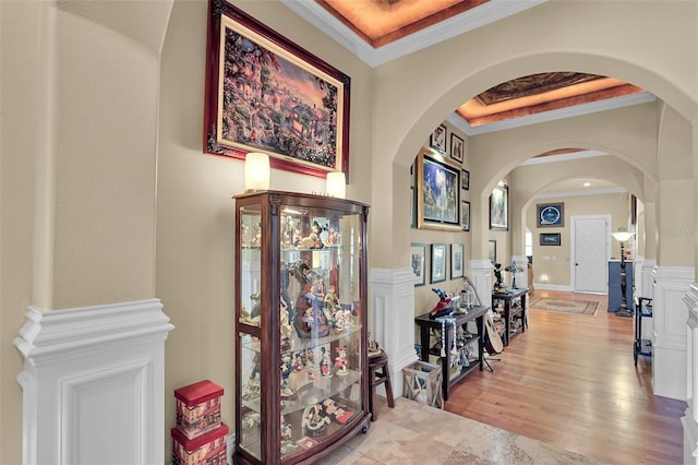 hallway with crown molding, wood finished floors, arched walkways, and a raised ceiling