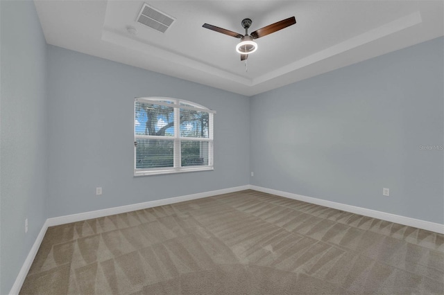 spare room featuring ceiling fan, light colored carpet, and a raised ceiling