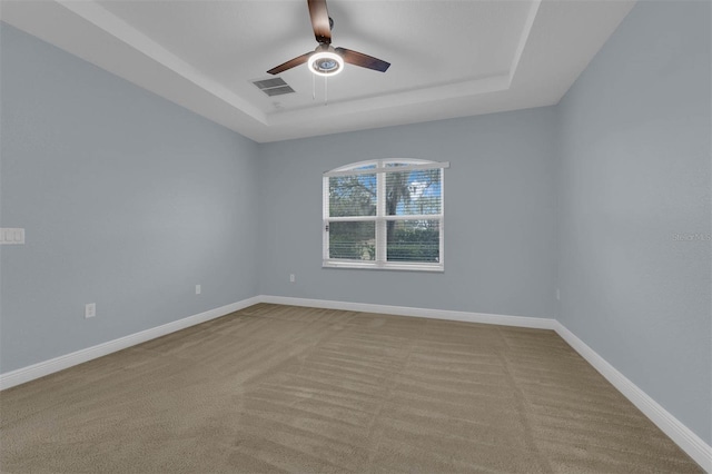 empty room featuring a tray ceiling, light colored carpet, and ceiling fan