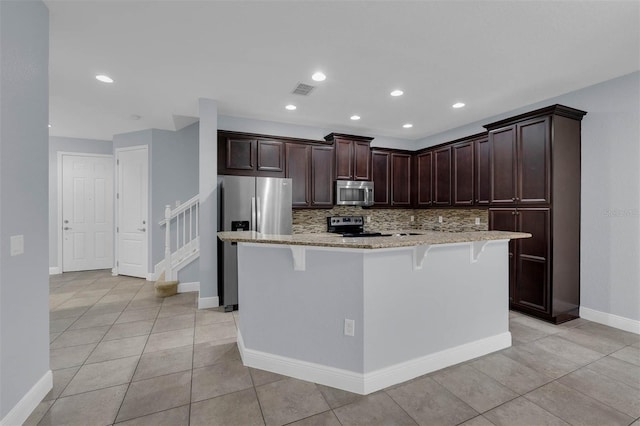 kitchen with a kitchen island, a breakfast bar, tasteful backsplash, stainless steel appliances, and dark brown cabinets