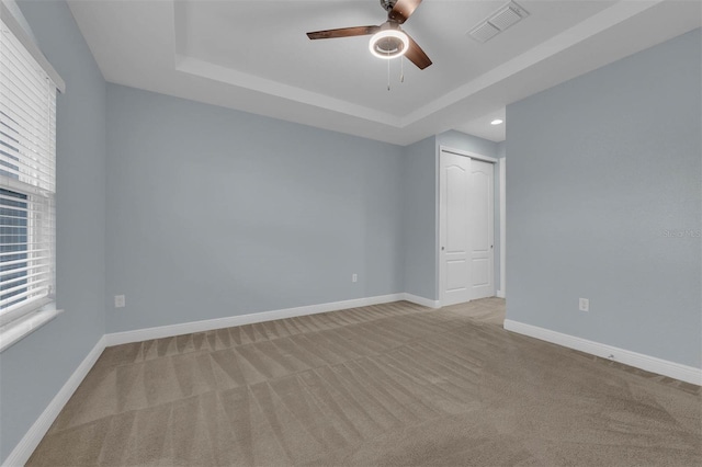 unfurnished room with light carpet, a tray ceiling, and ceiling fan