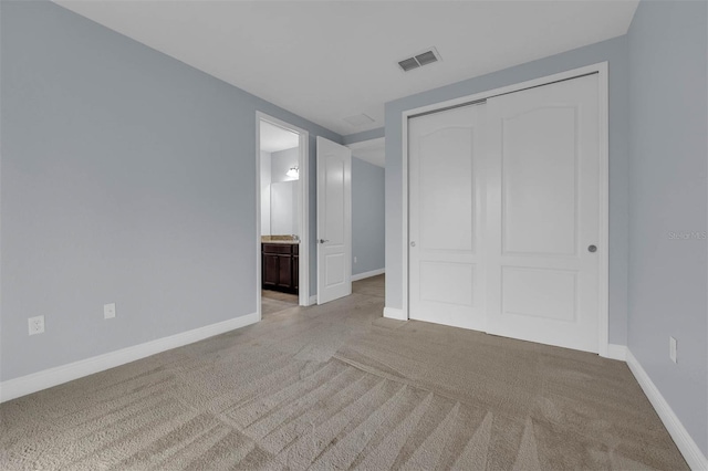 unfurnished bedroom featuring ensuite bath, light carpet, and a closet