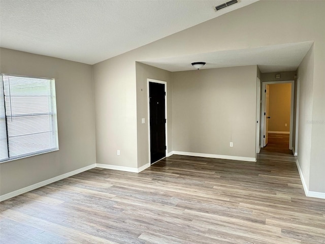 empty room featuring a textured ceiling, wood finished floors, visible vents, baseboards, and vaulted ceiling