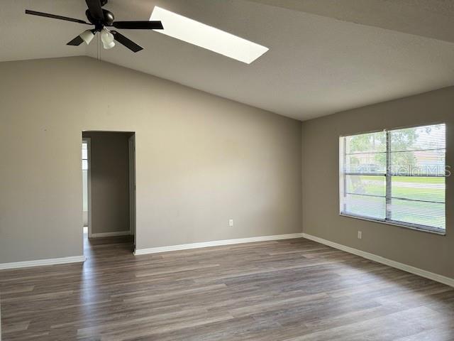 empty room featuring ceiling fan, hardwood / wood-style flooring, and vaulted ceiling with skylight