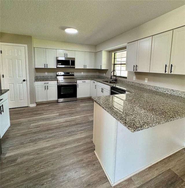 kitchen with stainless steel appliances, dark wood-type flooring, white cabinetry, a sink, and a textured ceiling