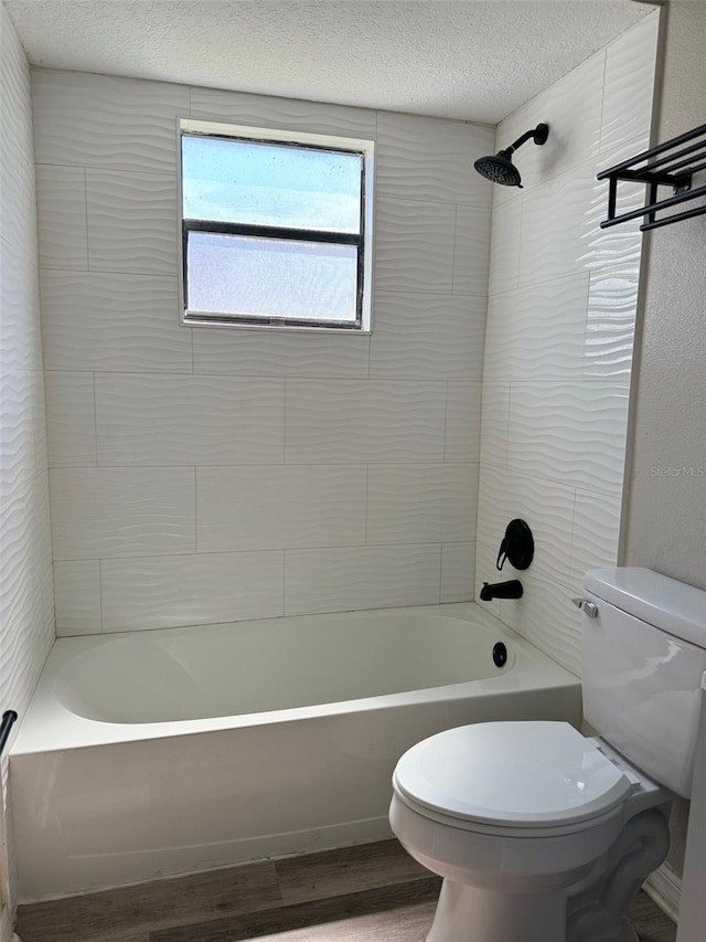 bathroom with hardwood / wood-style floors, tiled shower / bath combo, toilet, and a textured ceiling