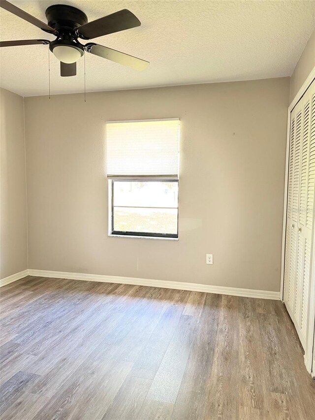 unfurnished bedroom featuring a textured ceiling, a closet, baseboards, and wood finished floors