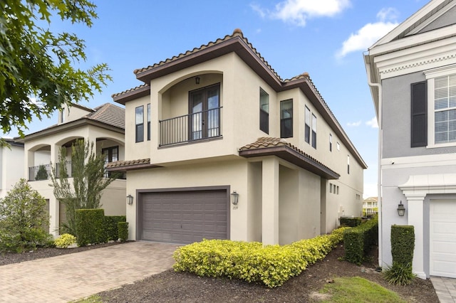 mediterranean / spanish-style home featuring a garage, a tiled roof, decorative driveway, and stucco siding