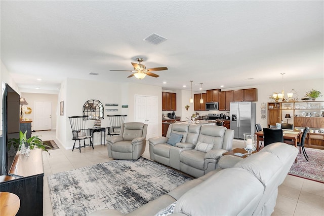 living room featuring a textured ceiling, light tile patterned flooring, and ceiling fan with notable chandelier